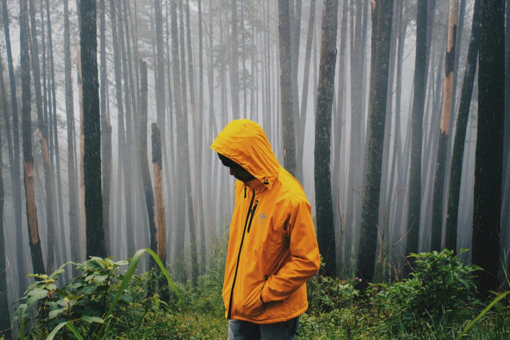 A man in a yellow jacket stands in a misty Indonesian forest, creating a serene and contemplative atmosphere.
